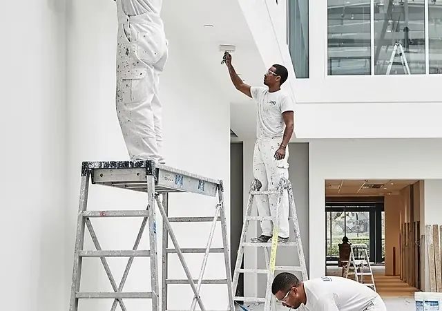 Painters on ladders and a rolling platform in a bright commercial space