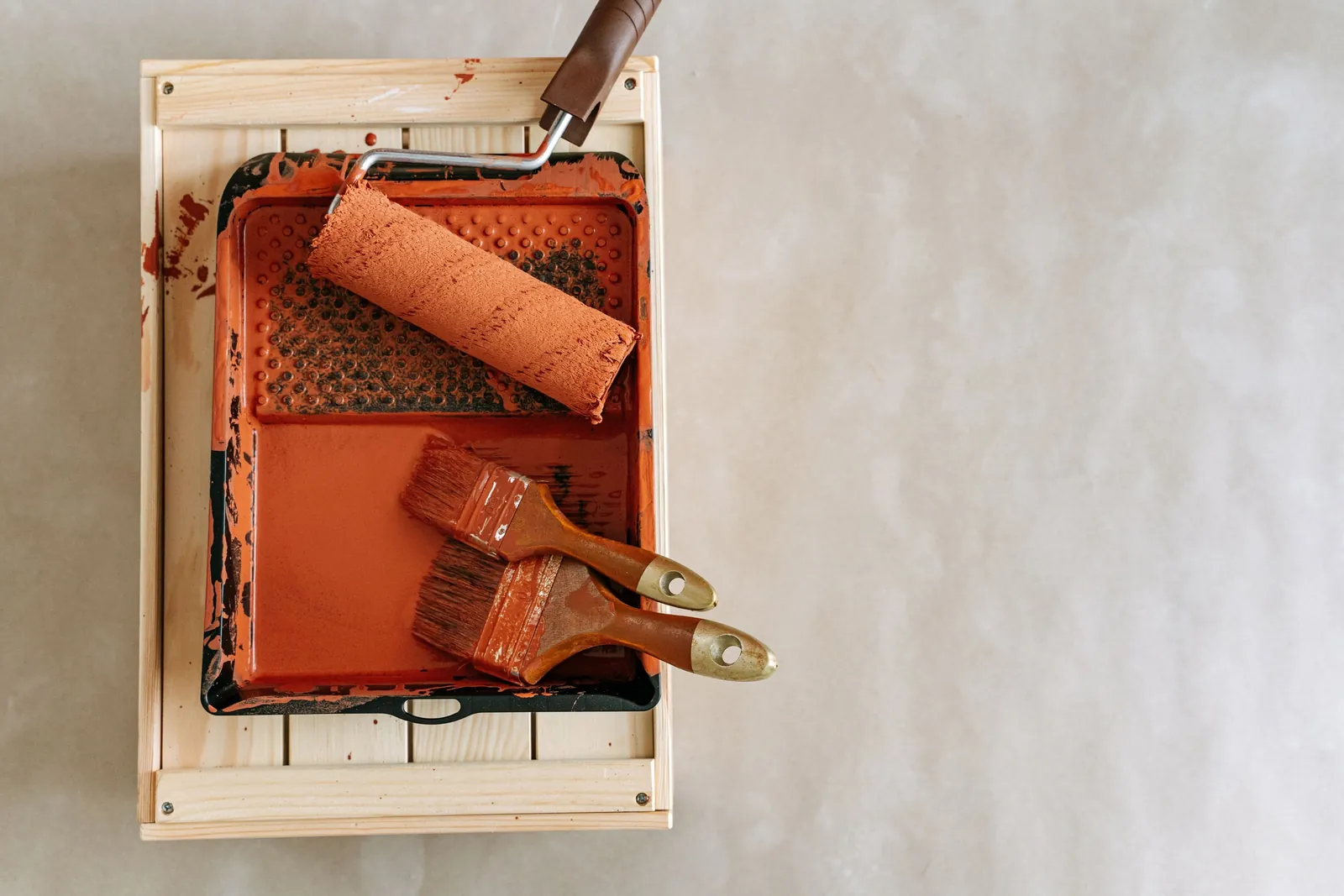 Paint roller and brushes in a tray of orange paint on a wooden crate